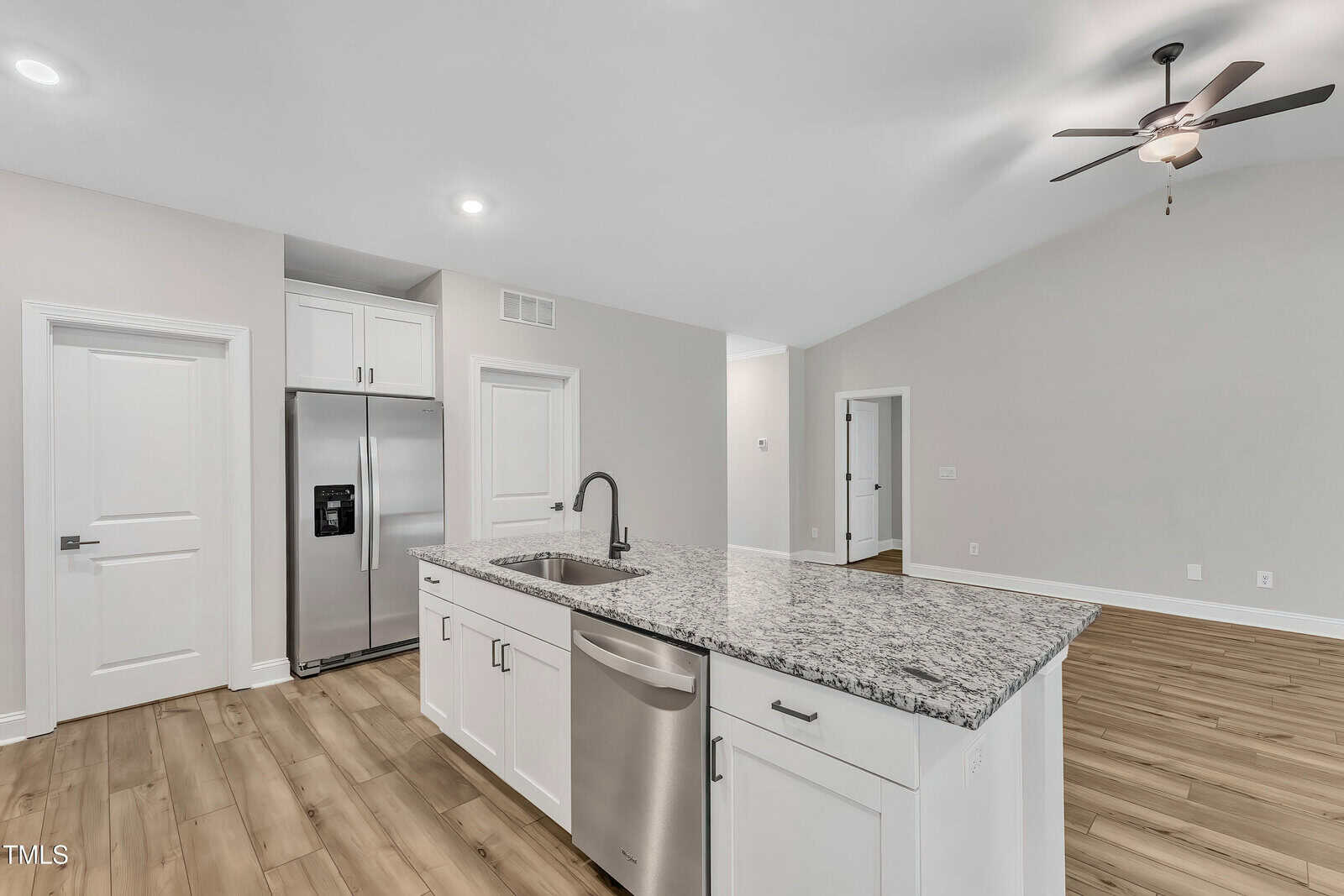 Modern kitchen with a granite island, stainless steel refrigerator, white cabinets, wood flooring, and a ceiling fan in an open, bright space.