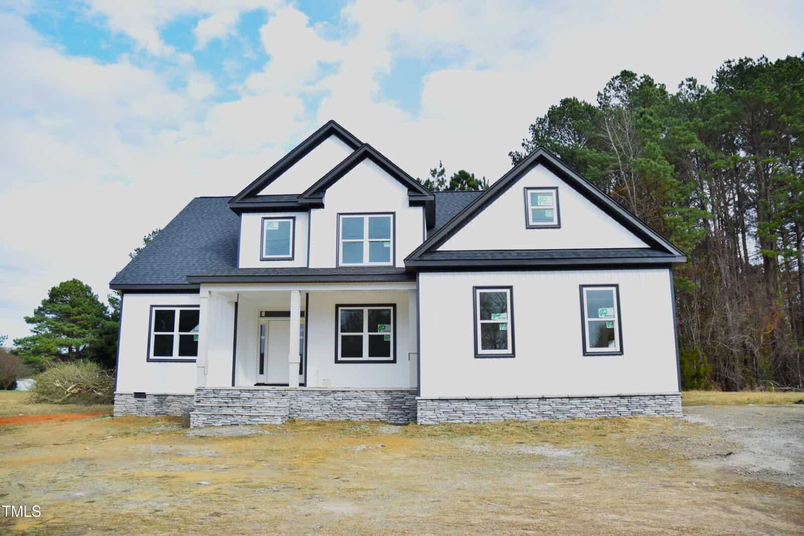 Set against a backdrop of trees in Franklinton, this newly constructed two-story house at 1586 Nc 96 Hwy features a combination of dark and light exterior trim, large windows, a covered front porch, and an elegant stone facade under a partly cloudy sky.