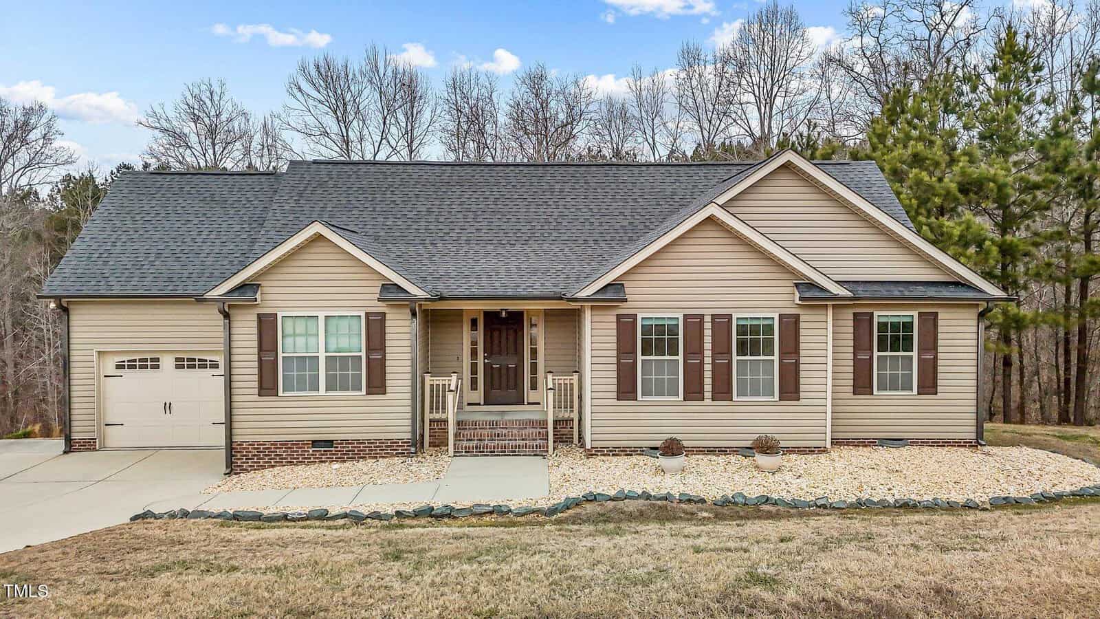 A charming single-story house at 131 Glasgow Street features a gable roof, beige siding, and brown shutters. With a garage on the left and a front porch at its stem, it boasts a landscaped garden with rocks, surrounded by lush grass and trees in the background.