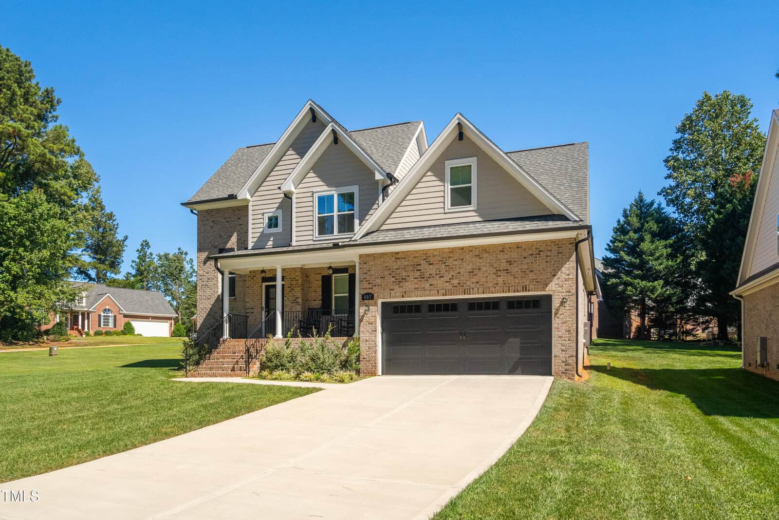 A charming two-story house at 407 Eagle Court in Henderson, showcasing a brick facade and gray siding. It features a large gable roof, a covered front porch, and a black garage door. The neatly trimmed lawn is set against a backdrop of trees and a clear blue sky.