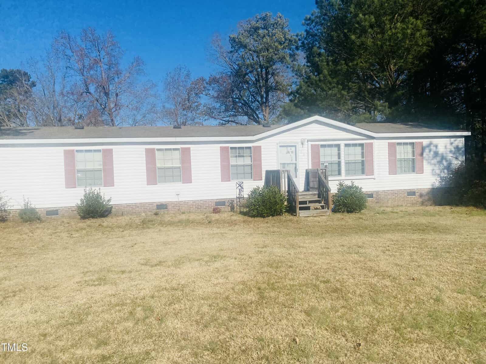 Nestled at 108 Madison Grove Ln in Henderson, this long, single-story white house boasts red shutters and a charming front door with a small porch and steps. It's set in a yard of lush grass and a few shrubs, surrounded by trees under the expansive blue sky.