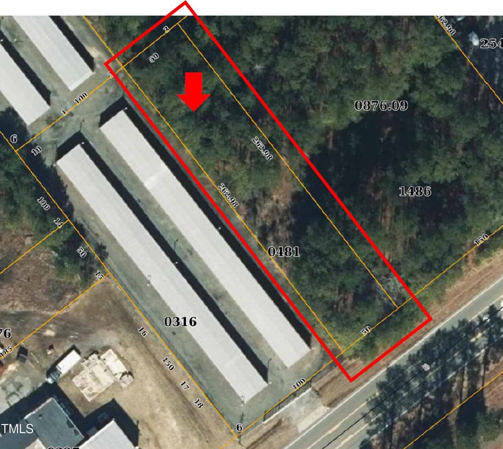 Aerial view of a storage facility complex with long, rectangular buildings. One building is outlined in red with an arrow pointing to it. Surrounding areas have trees and a road visible at the bottom right. Various numbers label sections of the image.