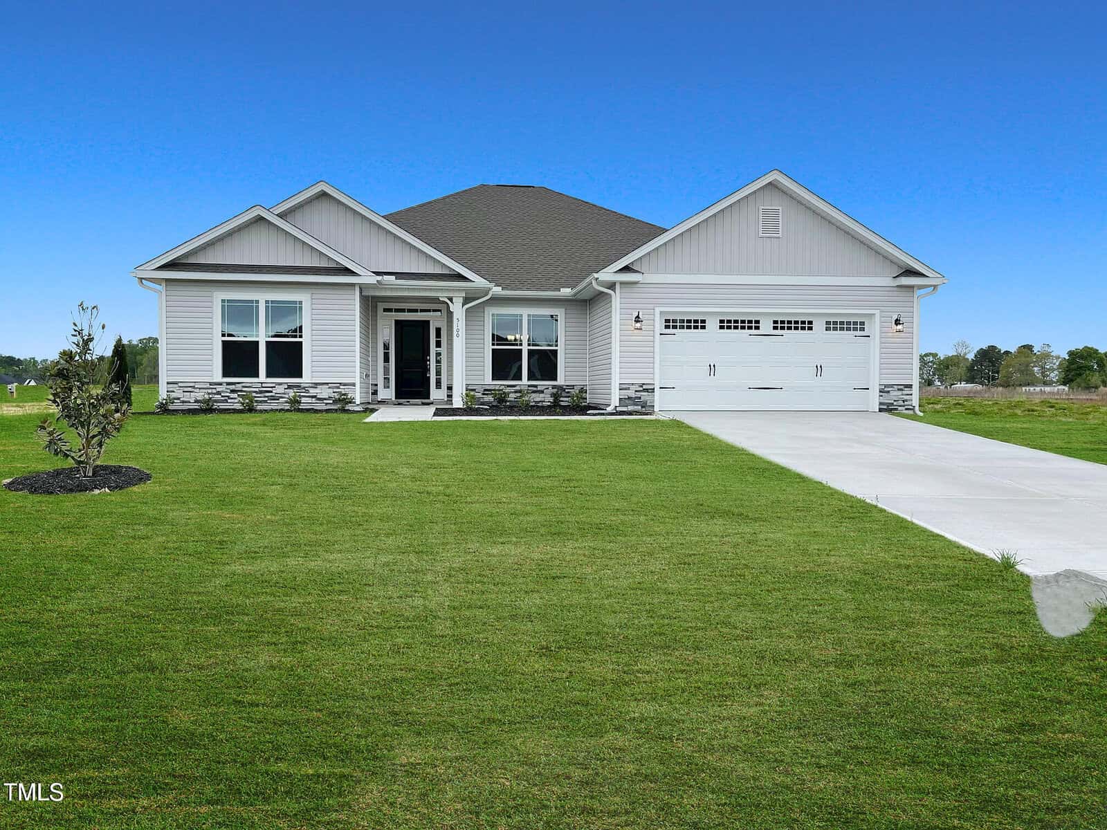 A single-story, modern suburban house with gray siding, a dark gray roof, two-car garage, and wide driveway, surrounded by a large, neatly mowed lawn under a clear blue sky.