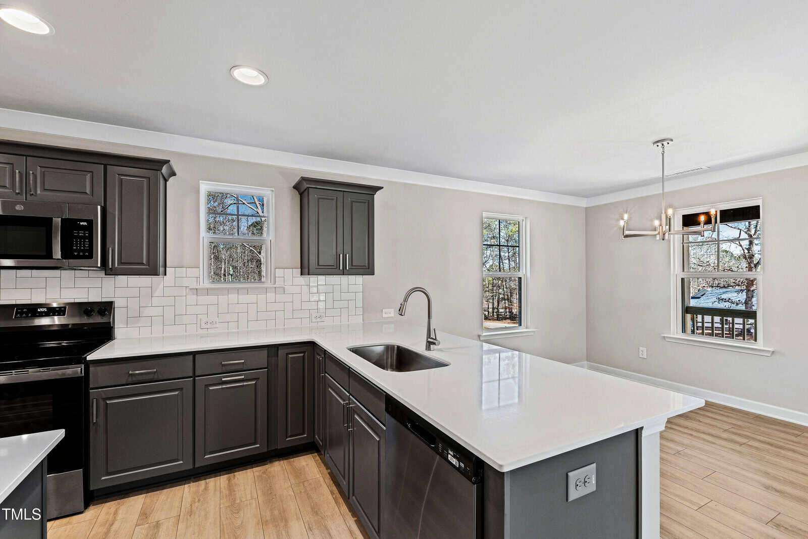 Modern kitchen with dark gray cabinets, white countertops, tile backsplash, stainless steel appliances, and an adjacent dining area with large windows letting in natural light.