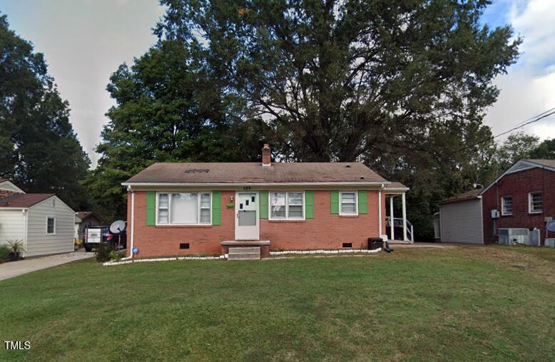 A single-story brick house at 829 Eastside Drive boasts green shutters and a white door, nestled on a grassy lawn in Henderson. A large tree stands proudly in the background, flanked by neighboring homes. The sky above is partly cloudy, adding to the serene setting.
