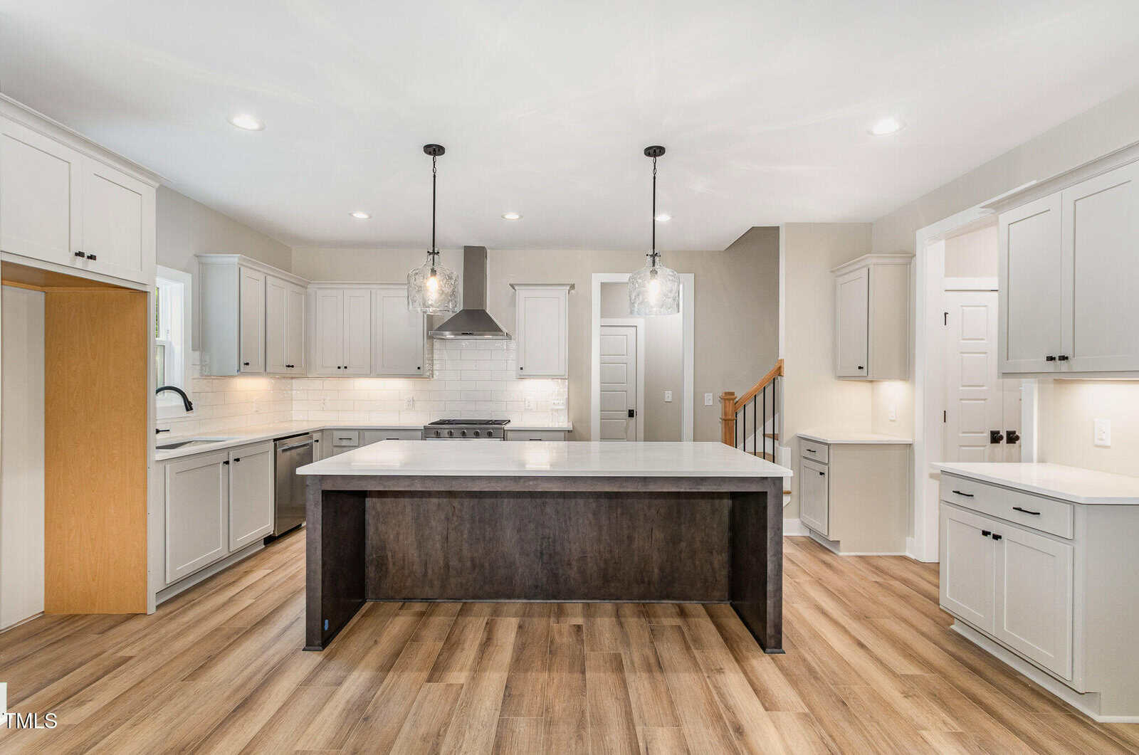 Modern kitchen with white cabinets, stainless steel appliances, a large island with dark wood base and light countertop, pendant lighting, wood floors, and white subway tile backsplash.