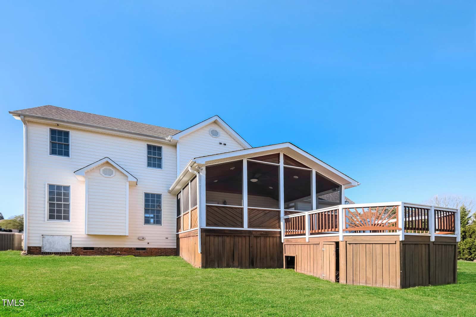 A two-story white house with a screened porch and elevated wooden deck, set against a clear blue sky. The yard is grassy, and the house has multiple windows on the back side.