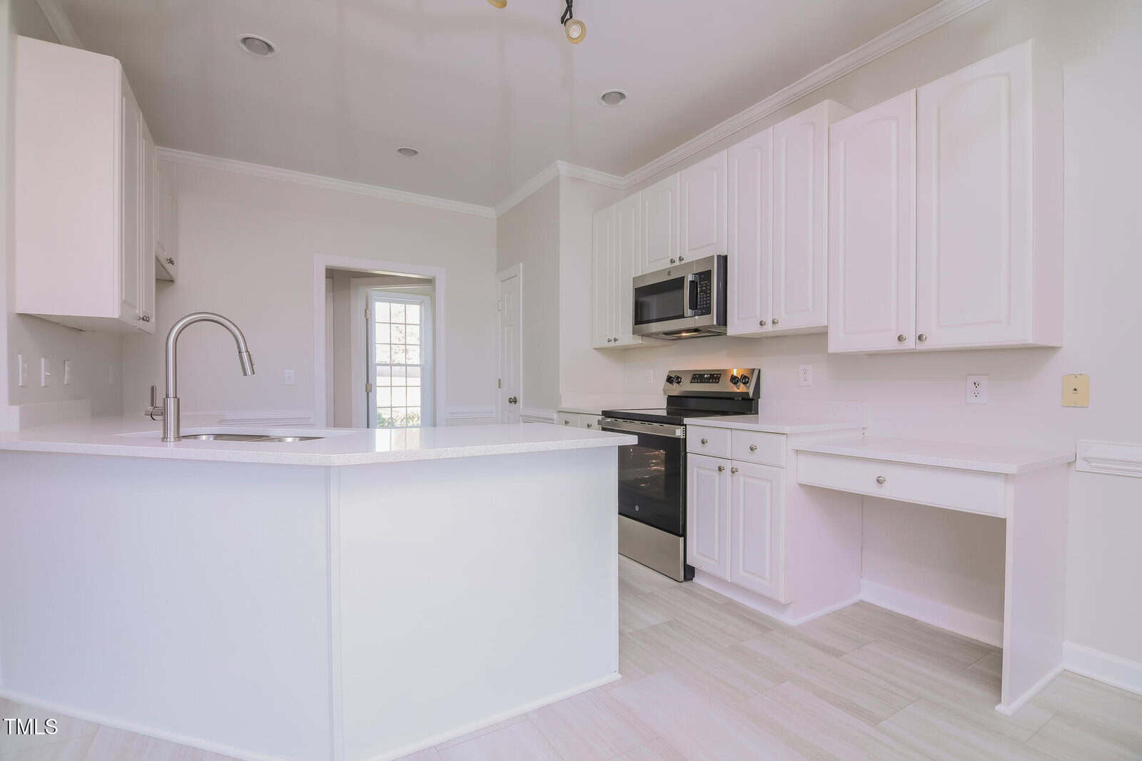 A modern kitchen with white cabinets, a stainless steel oven and microwave, and a center island with a sink. The room has a neutral color palette and tile flooring. There is a doorway leading to another space in the background.