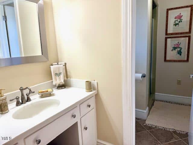 A bathroom with a white sink vanity, silver faucet, and a mirror above. The countertop has a soap dispenser, a soap dish, and a towel with a butterfly design. In the background, there is an open door leading to another room with floral wall art.