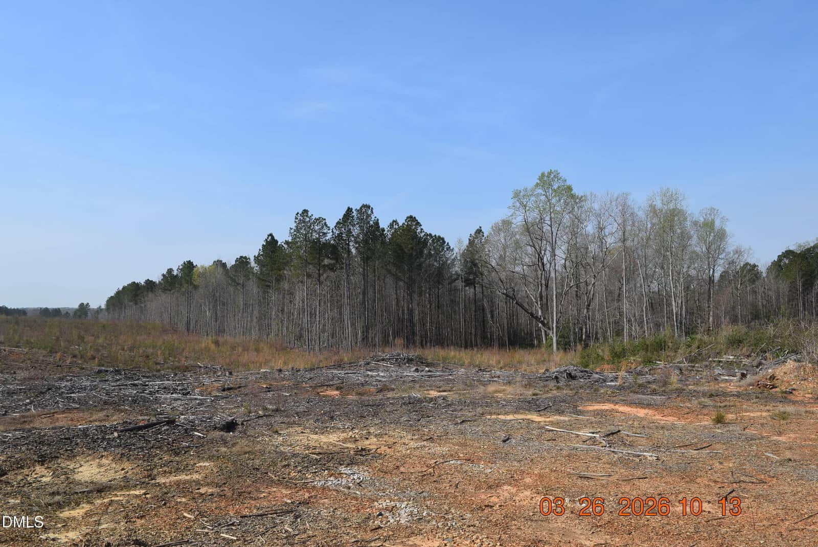 A cleared, barren patch of land with scattered debris is in the foreground, bordered by a dense line of trees under a clear blue sky. The date “08-26-2020” is visible in the bottom right corner.