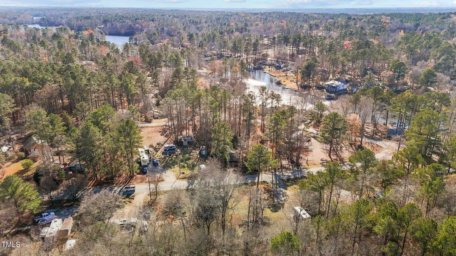 Aerial view of a wooded lakeside area with scattered RVs and mobile homes, a road running through the foreground, and a body of water seen in the background among trees.