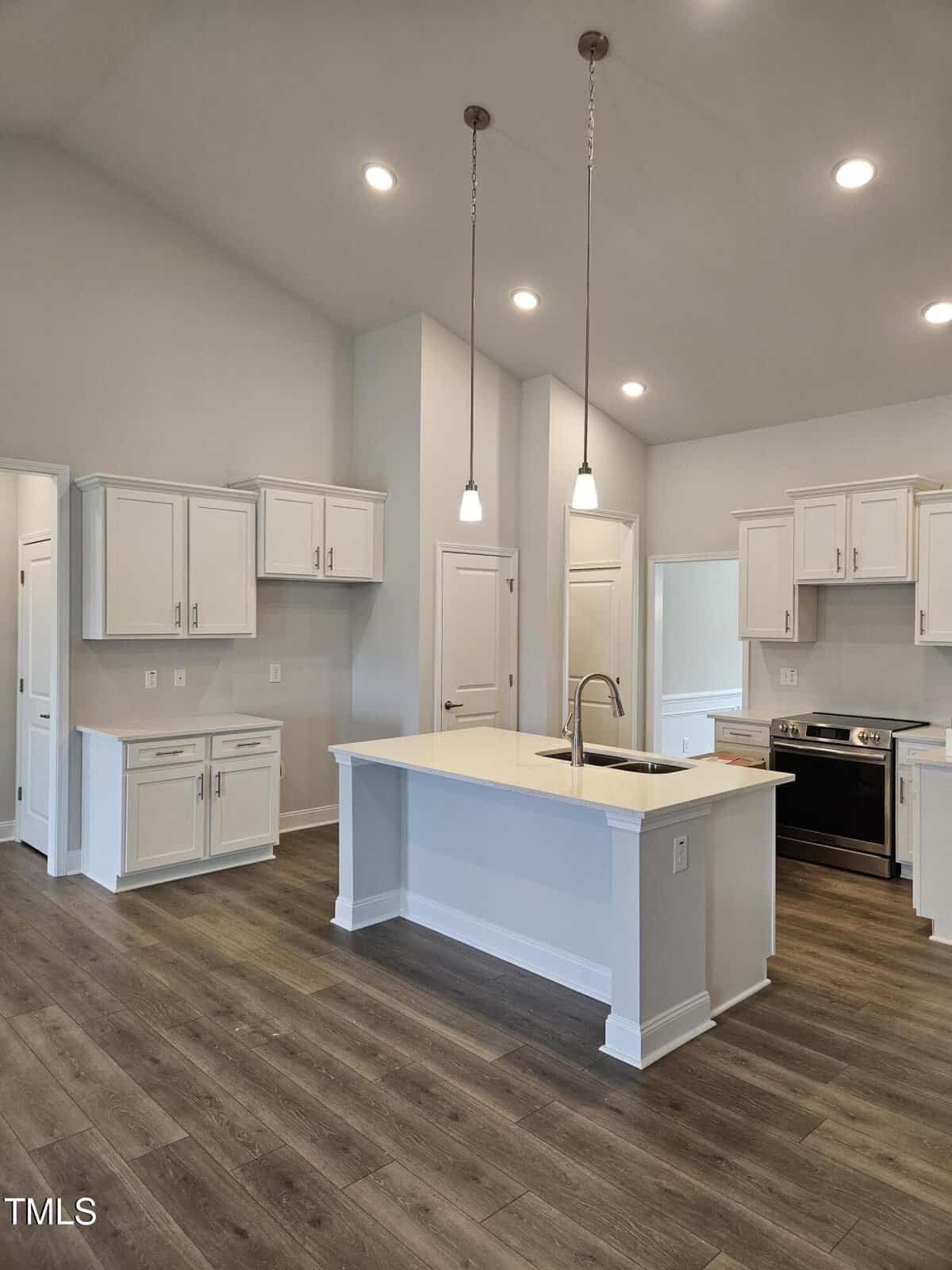 Modern kitchen with white cabinets, stainless steel appliances, an island with a sink and pendant lights, and wood-look flooring. The space is bright with recessed lighting and neutral walls.
