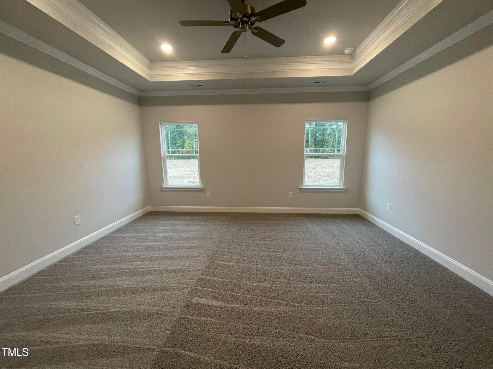 Empty carpeted room with two windows, tray ceiling with recessed lighting, ceiling fan, and neutral-colored walls. Sunlight comes through the windows, illuminating the clean space.