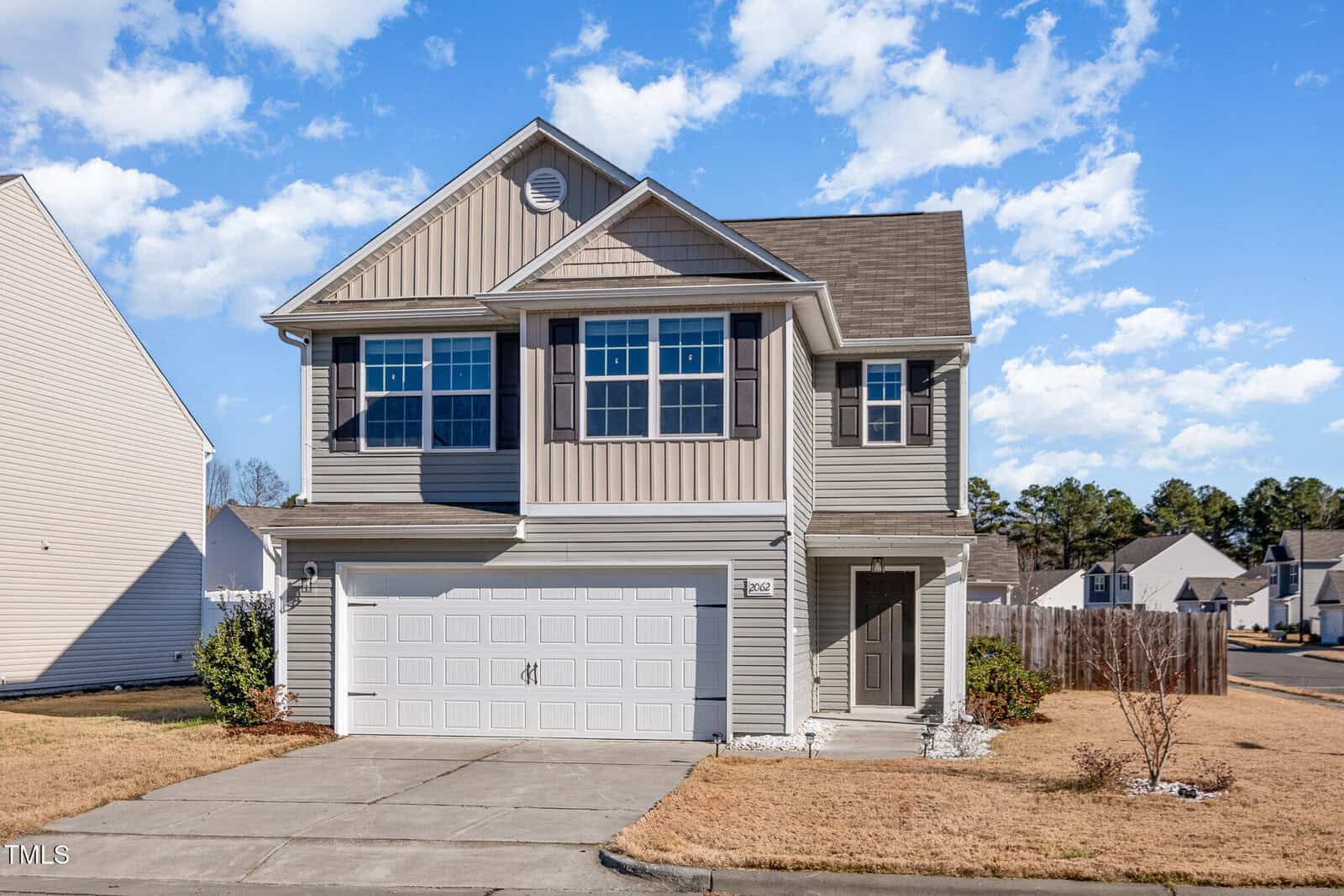 This charming two-story suburban house on 2062 Alderman Way in Creedmoor boasts beige siding, dark shutters, and a gable roof. A two-car garage flanks the right, while a wooden fence edges the brown lawn. The sky is clear with a few clouds, accentuating its inviting curb appeal.