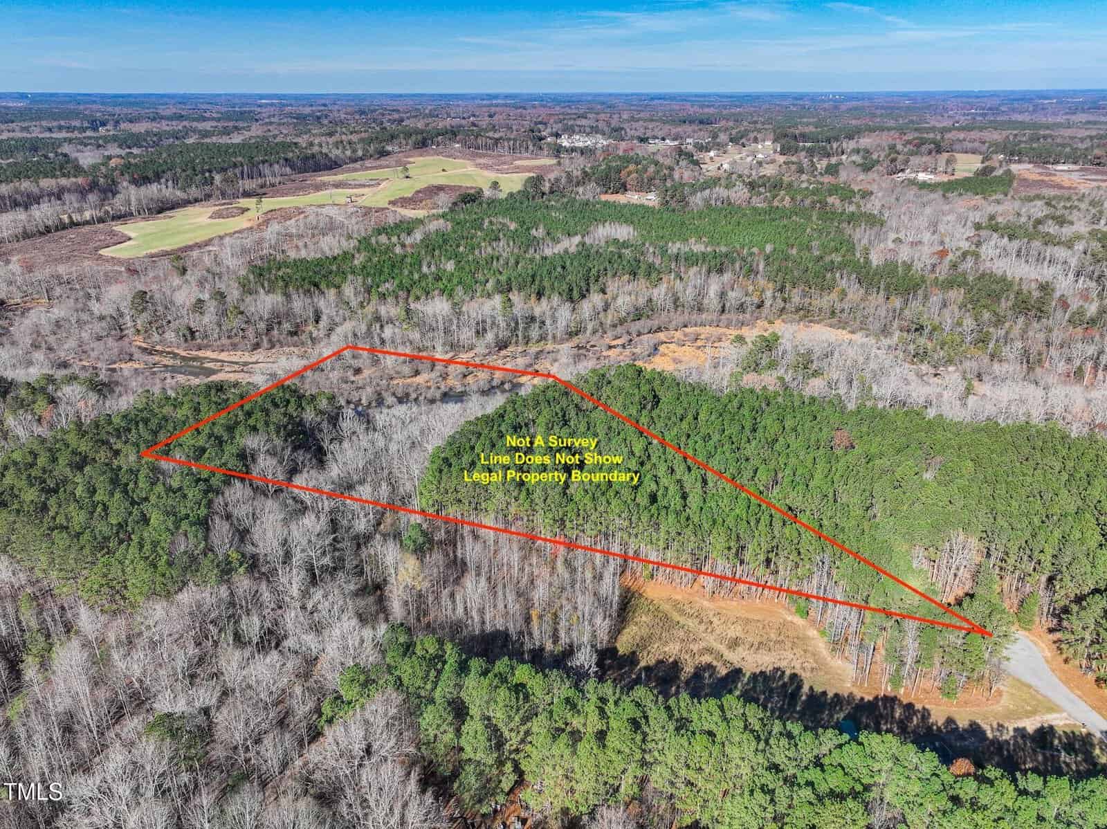 Aerial view of a wooded area with a red outline marking a section of land. Text inside the outline reads, "Not a survey. Line does not show legal property boundary." A road runs along the lower right edge.