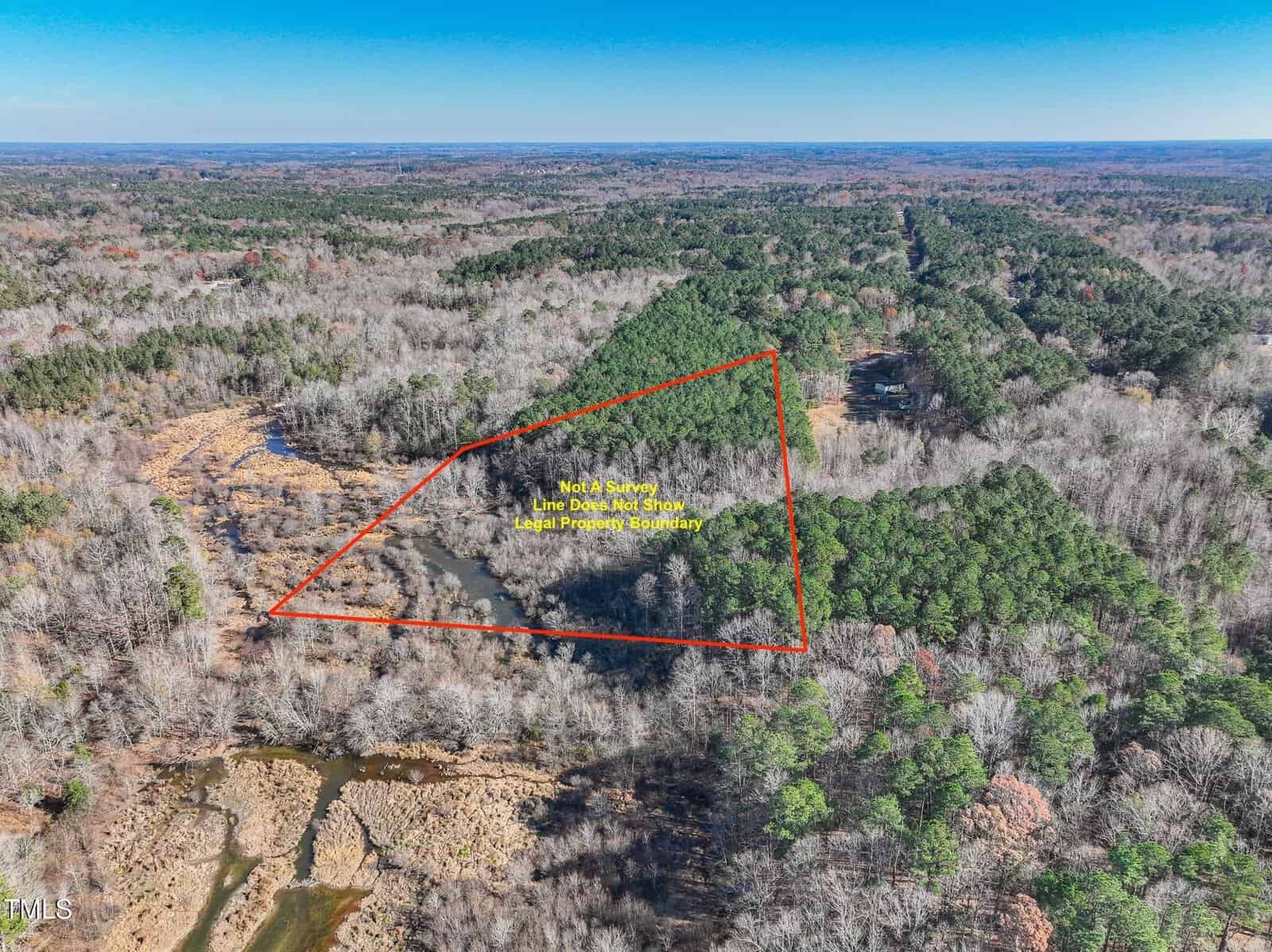 Aerial view of a wooded area with a triangular plot outlined in red, labeled as “Not a Survey, Line Depicts Approx Legal Property Boundary,” surrounded by trees and a stream in the bottom left corner.