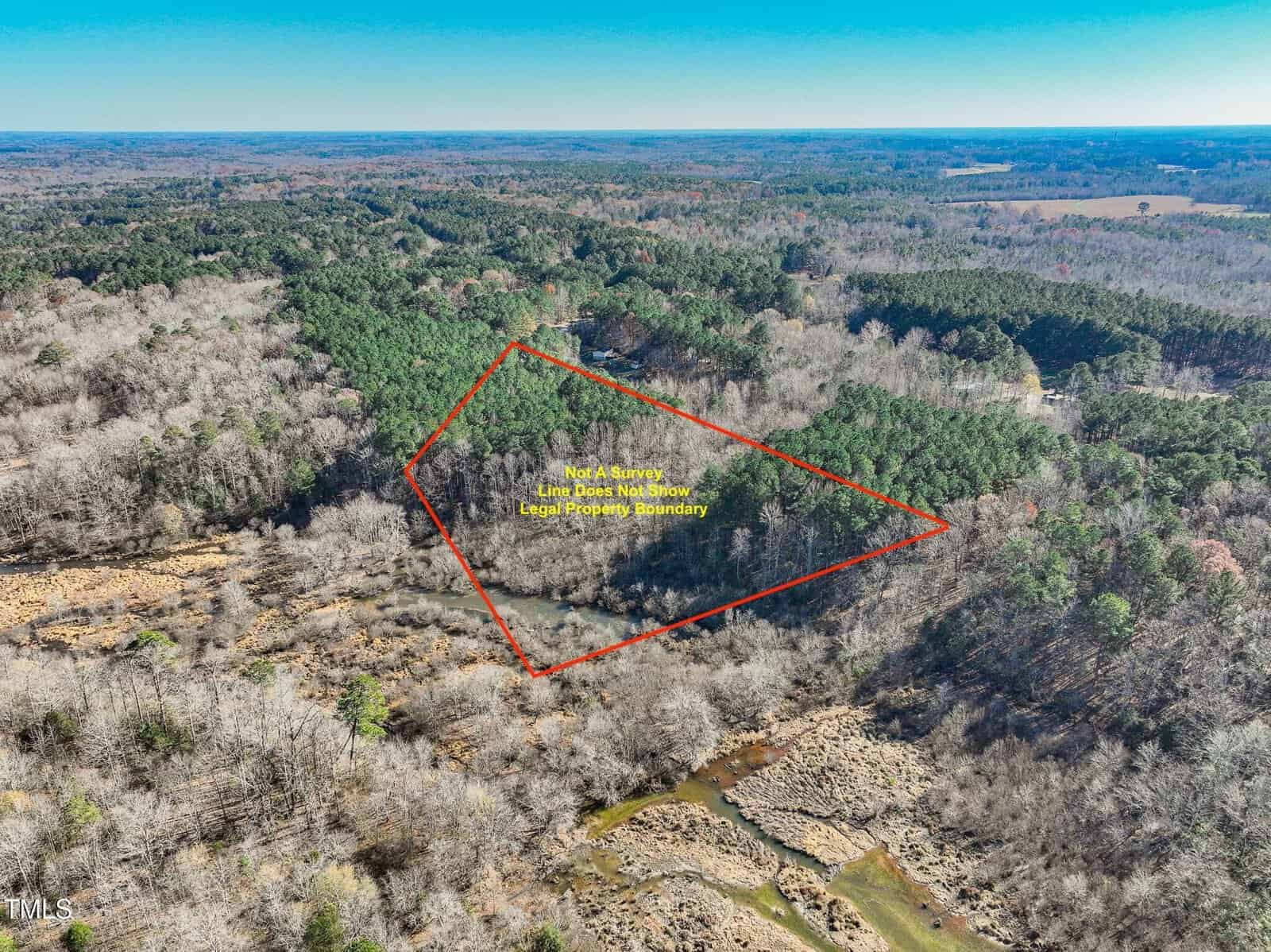 Aerial view of a forested area with a red outlined triangle indicating approximate property boundaries; surrounding land features a mix of trees, grass, and a visible creek. Text notes: "Not a Survey. Line for illustration only. Not legal property boundary.