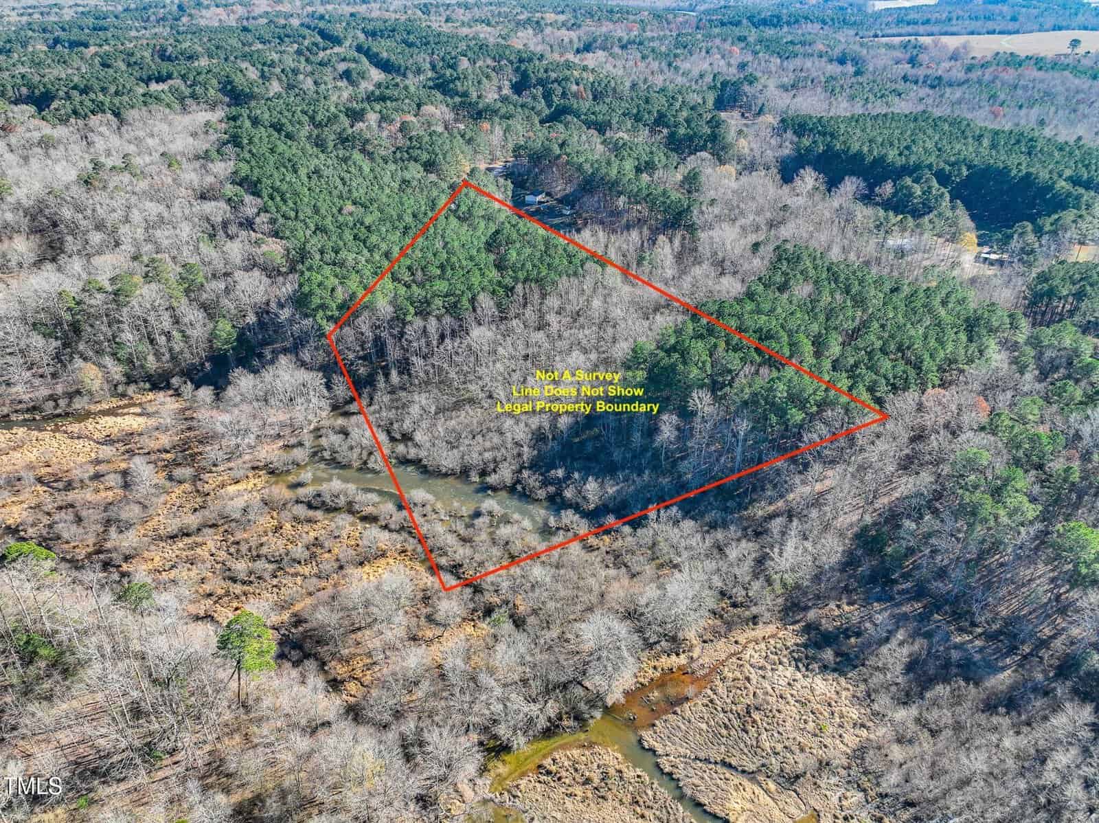 Aerial view of wooded land, outlined in red to show legal property boundary, with a creek running through the area, surrounded by forest and open patches. Text labels the outlined land within the image.
