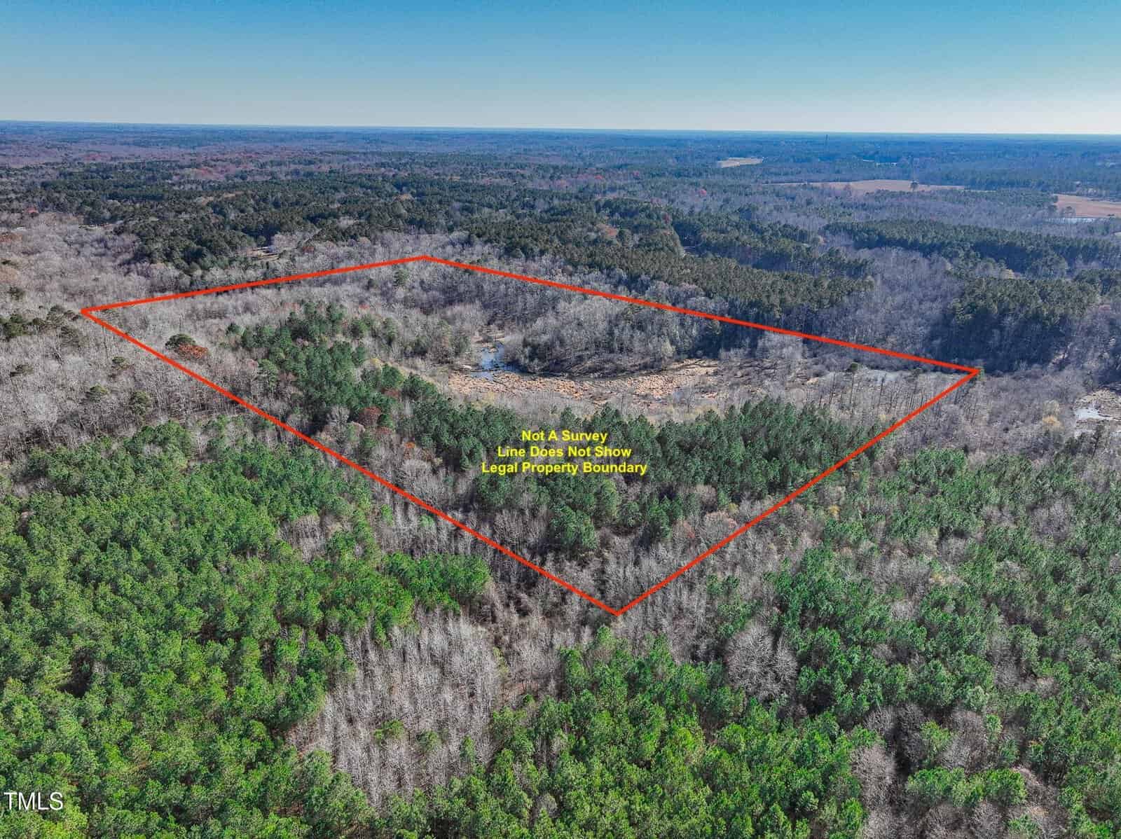 Aerial view of a large, wooded area with a red outline indicating the property boundary. The text inside the outlined area states, "Not a survey line does not show legal property boundary." Forests surround the land.