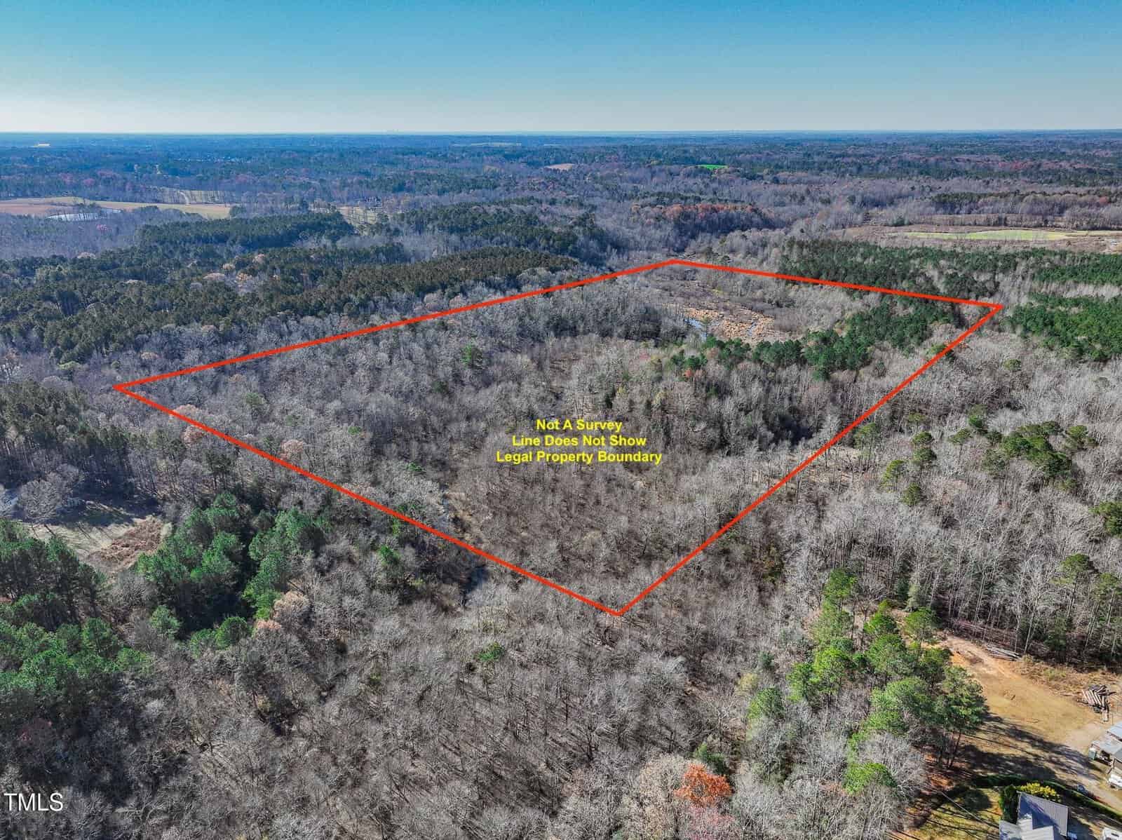 Aerial view of a wooded area with a red outline marking the approximate boundary of a property. Text inside the outline notes that line dots do not show the legal property boundary. Surrounding forest and clearings are visible.
