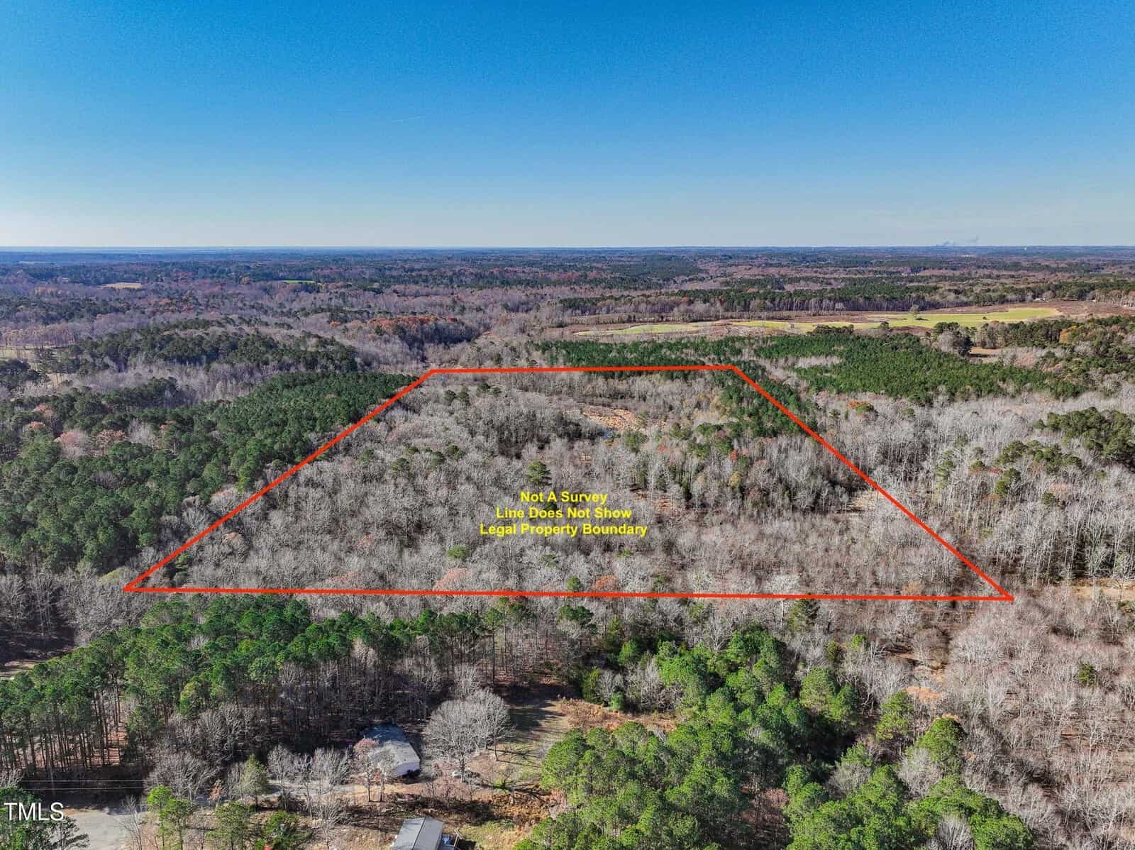Aerial view of a large wooded area with a red outline marking the approximate property boundary. The land is surrounded by forests and open fields under a clear blue sky. Text overlay notes it is not a survey.