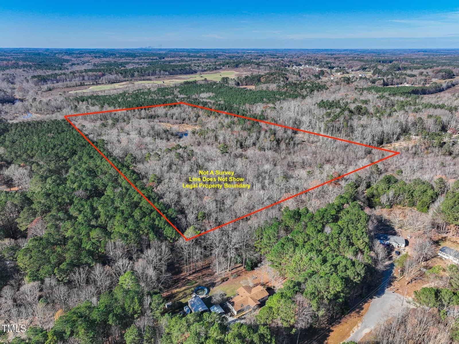 Aerial view of a large, wooded area outlined in red, indicating approximate property boundaries. The land is surrounded by dense trees and a few houses are visible near the bottom edge of the image.