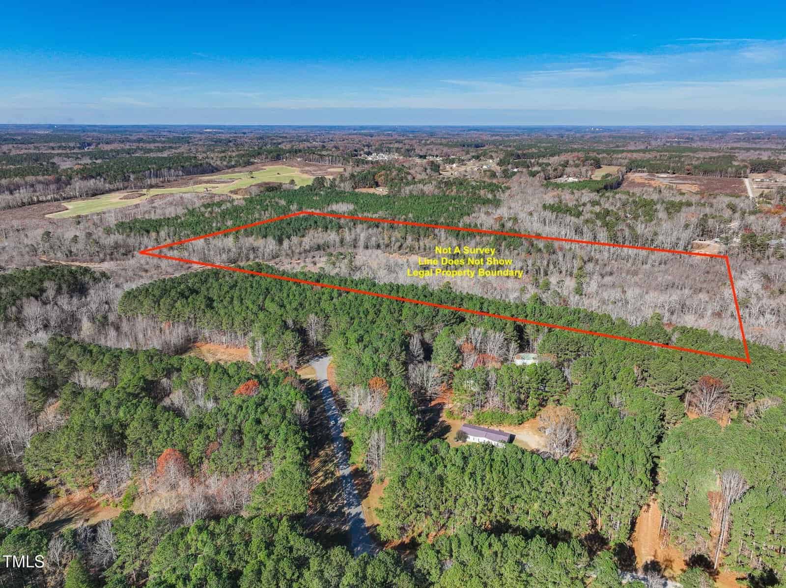 Aerial view of a large wooded land plot outlined in red, with surrounding trees, clearings, and distant landscape under a clear blue sky. Yellow text appears inside the outlined area.