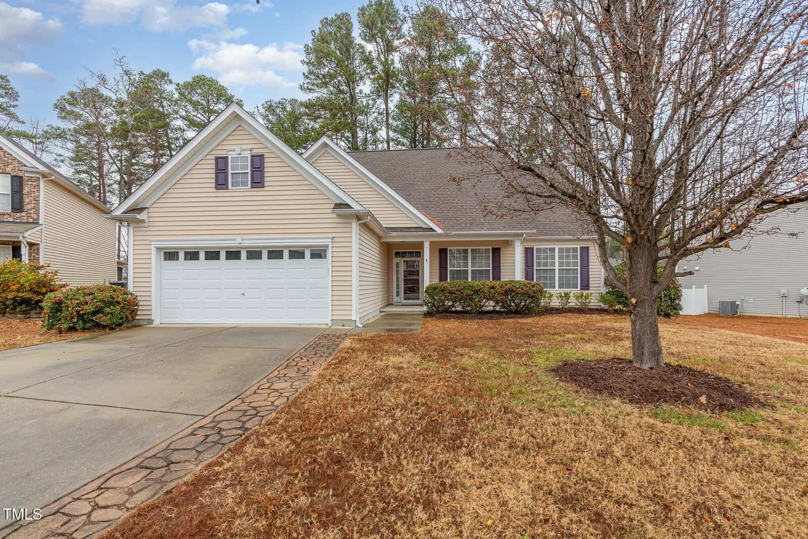 Located in the charming Creedmoor neighborhood, this suburban single-story house at 2204 Regent Court boasts beige siding and a gray roof. It features a two-car garage, a covered front porch, and a leafless tree in the front yard. The driveway and walkway showcase an elegant decorative stone pattern.