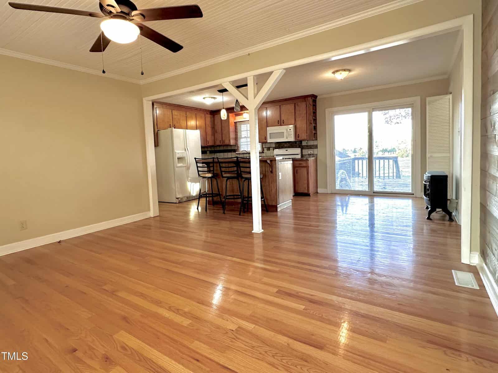 Open floor plan with hardwood floors, a ceiling fan, and a kitchen area featuring wooden cabinets and bar seating. Sliding glass doors lead to a deck, bringing in natural light.