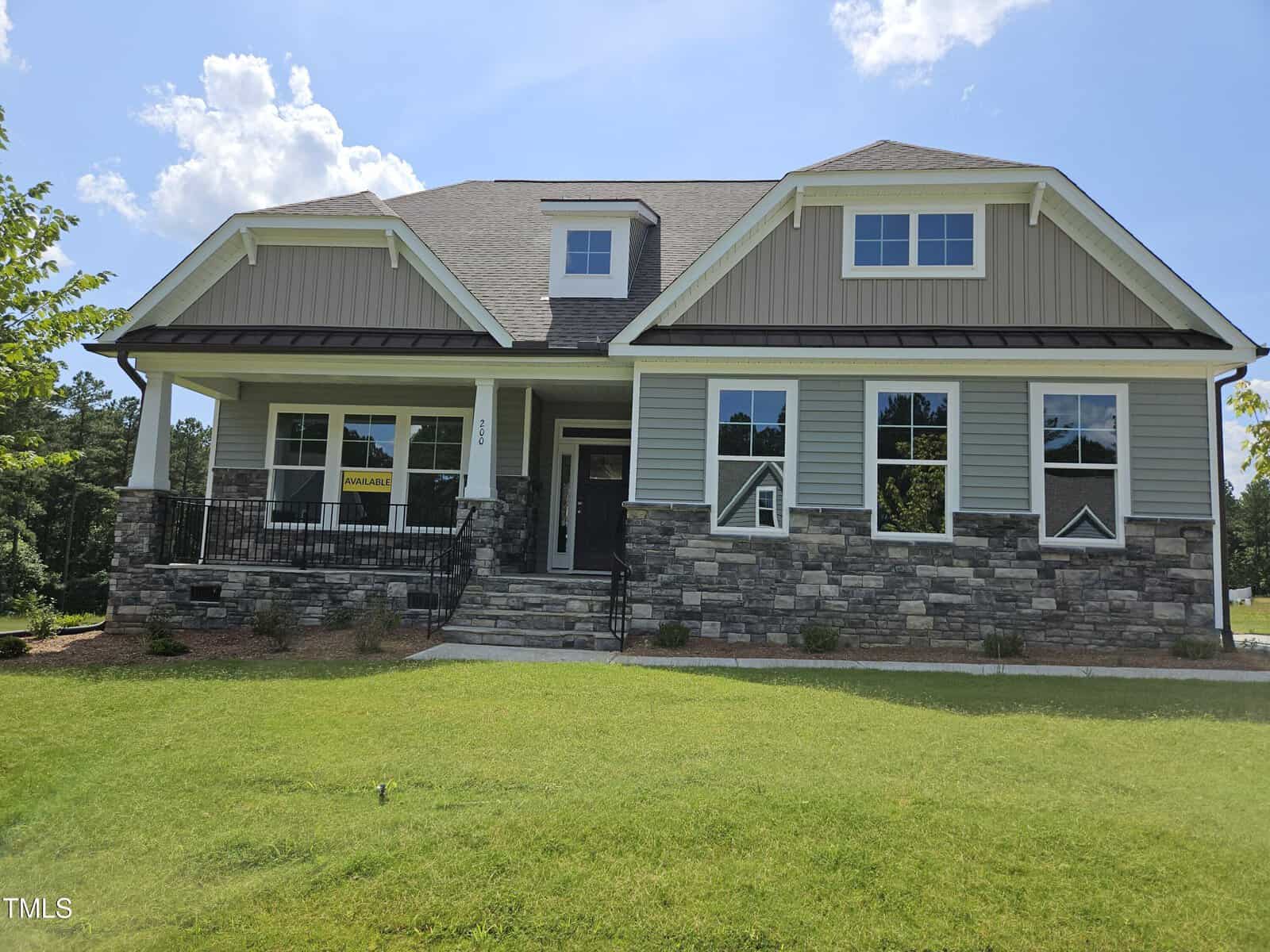 A single-family house with gray siding, stone accents, and a covered front porch is located at 200 Ironwood Boulevard in Youngsville. Multiple large windows are visible, and a “for sale” sign is in one window. The house sits on a grassy lawn with minimal landscaping.