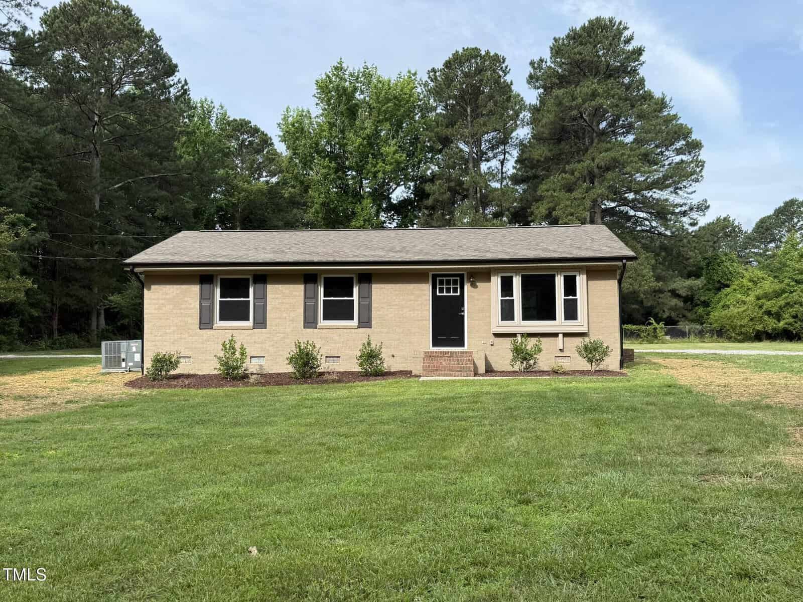 This single-story brick house at 2253 Nc Highway 96 in Franklinton features a dark roof, five front windows, a centered black door, and small shrubs along the front. It sits on a well-maintained lawn with trees in the background.