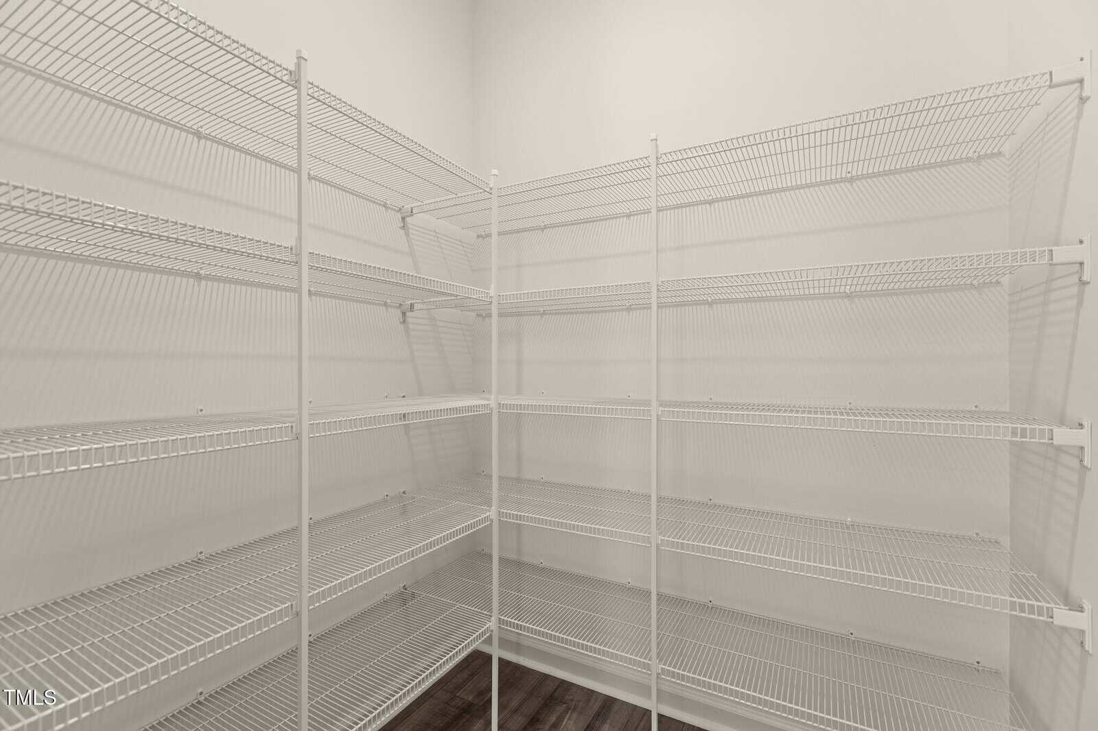 A walk-in pantry with white wire shelving units on two walls, empty shelves, white walls, and dark wood flooring.