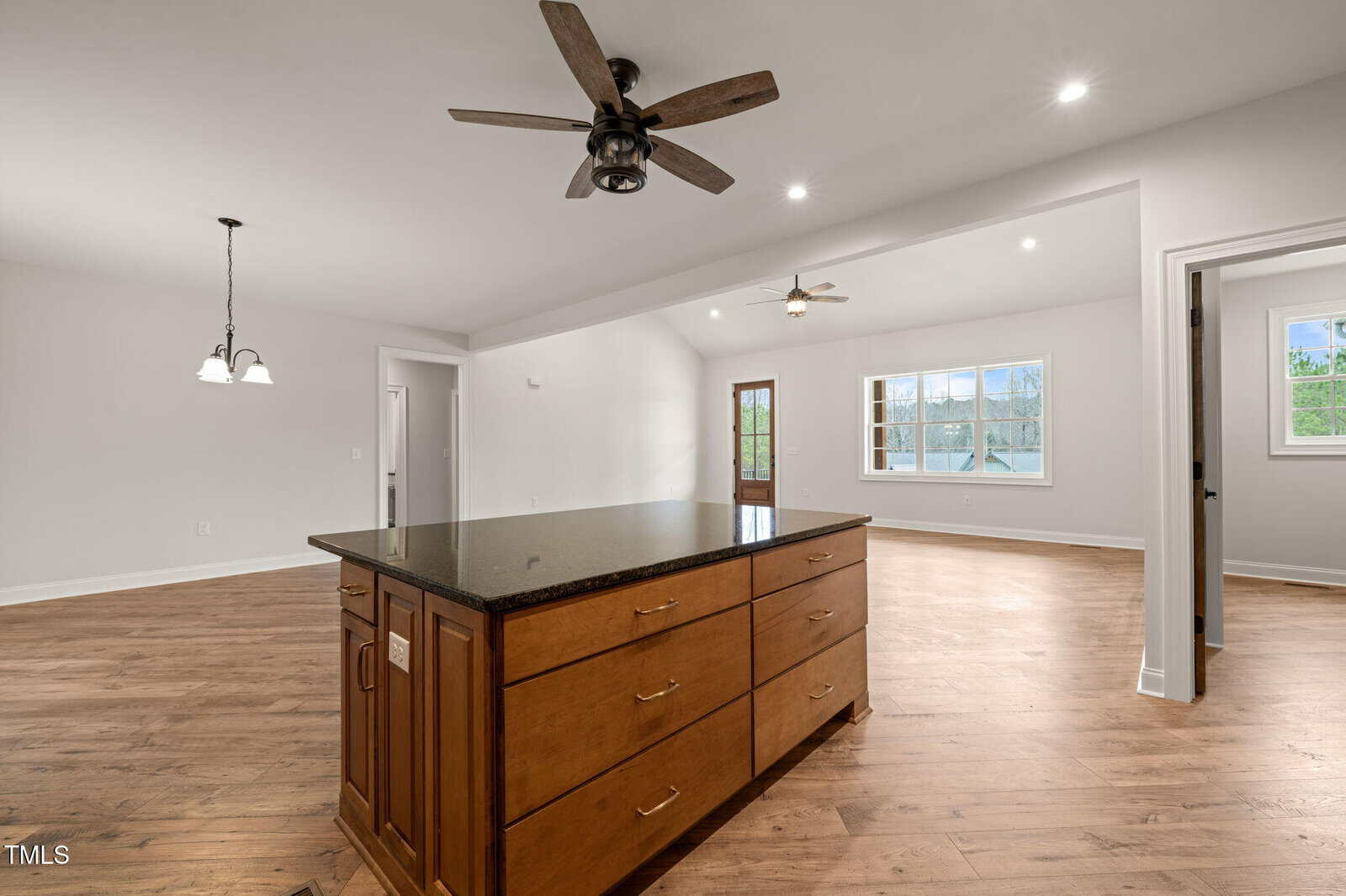 Spacious open-concept kitchen and living area with wood floors, an island with drawers, ceiling fans, pendant lights, and large windows letting in natural light.