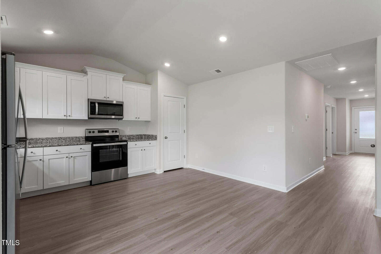 Modern kitchen with white cabinets, stainless steel appliances, and light wood flooring. The room opens to a hallway leading to a door with frosted glass. Ceiling lights are evenly spaced, and a closet door is visible to the right.