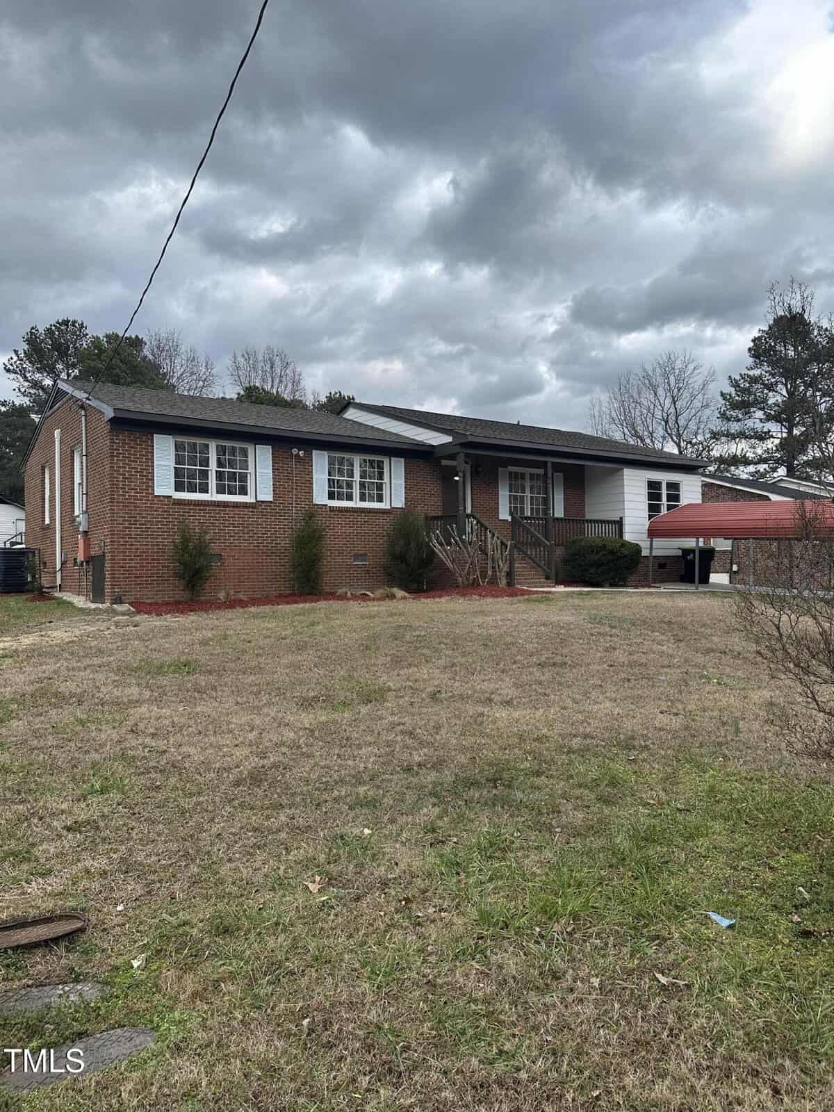 A brick house with a sloped roof, front steps, and a small porch is situated in a yard with sparse grass. A tree is on the right, and the sky above is cloudy, creating a gray atmosphere.