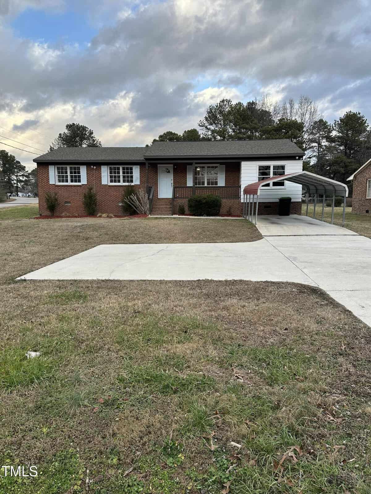 A charming single-story brick house at 1101 Water Street in Henderson is shown. It features a white trim, grassy front yard, concrete driveway, and a carport. The sky is partly cloudy, with trees in the background completing the picturesque setting.
