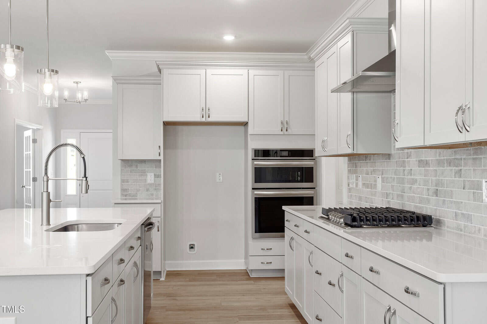 Modern kitchen with white cabinets, stainless steel appliances, a built-in oven, gas cooktop, tile backsplash, quartz countertops, island with sink, and wooden floor. Room is well-lit with recessed and pendant lights.