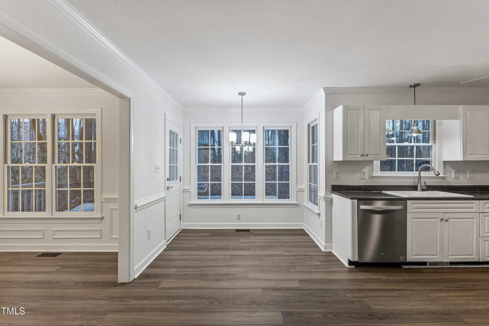 Bright kitchen and dining area with large windows, white cabinets, stainless steel appliances, and wood flooring. Natural light fills the space, creating an open, modern, and inviting atmosphere.