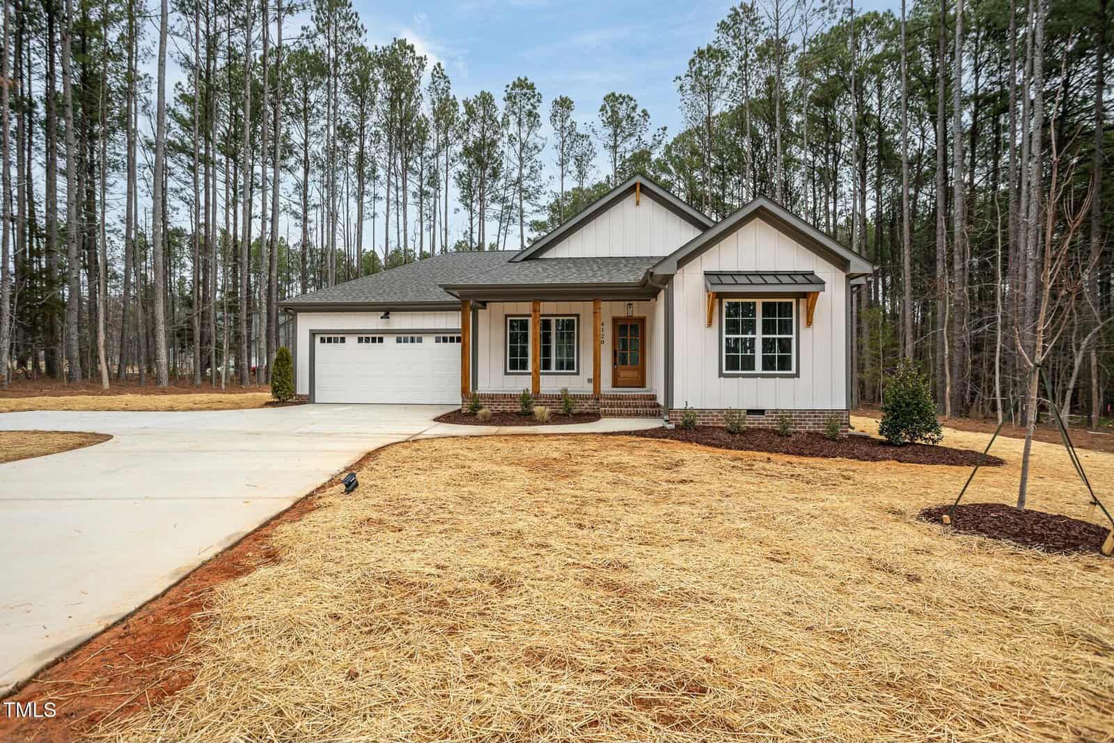 Set against a backdrop of tall pine trees, this single-story house at 4120 Emily Lane features gray siding and a charming covered front porch. With a two-car garage and newly paved driveway, the Oxford residence also boasts fresh landscaping with straw covering the front yard.