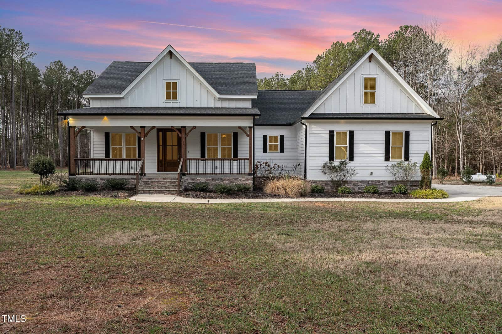Nestled at 95 Somerset Lane, this charming white house in Henderson features a black roof and a wooden front porch, surrounded by lush grass and sparse landscaping. The sky above dazzles with hues of pink and purple, while trees stand gracefully in the background.