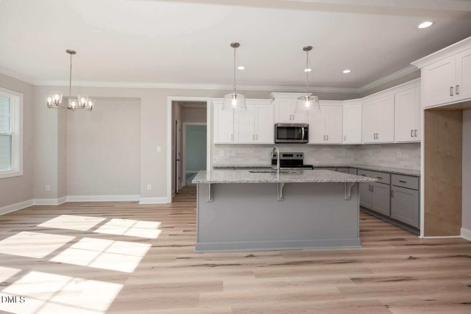 Modern kitchen with white cabinets, stainless steel appliances, granite countertops, and a large island with pendant lighting. Adjacent dining area with windows and a chandelier, light wood floors throughout.