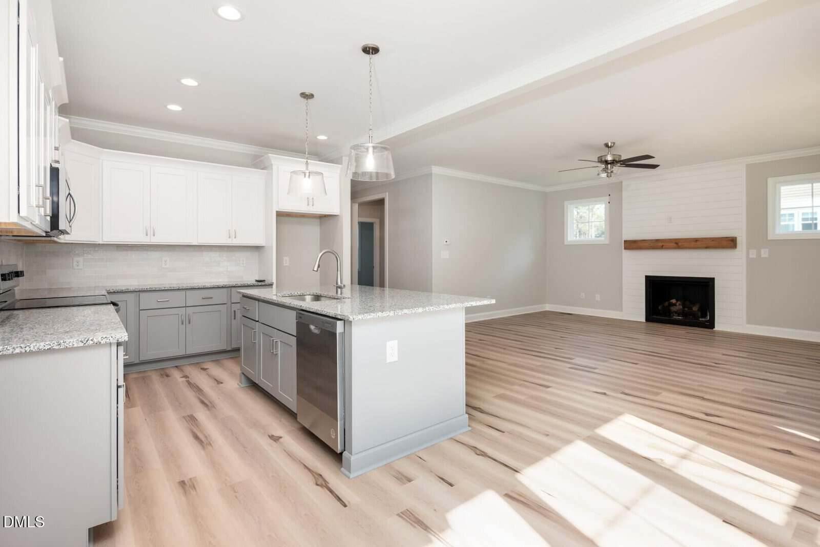 Modern kitchen with gray cabinets, granite countertops, a large island, and stainless steel appliances, open to a bright living area with wood floors, a ceiling fan, a fireplace, and large windows.