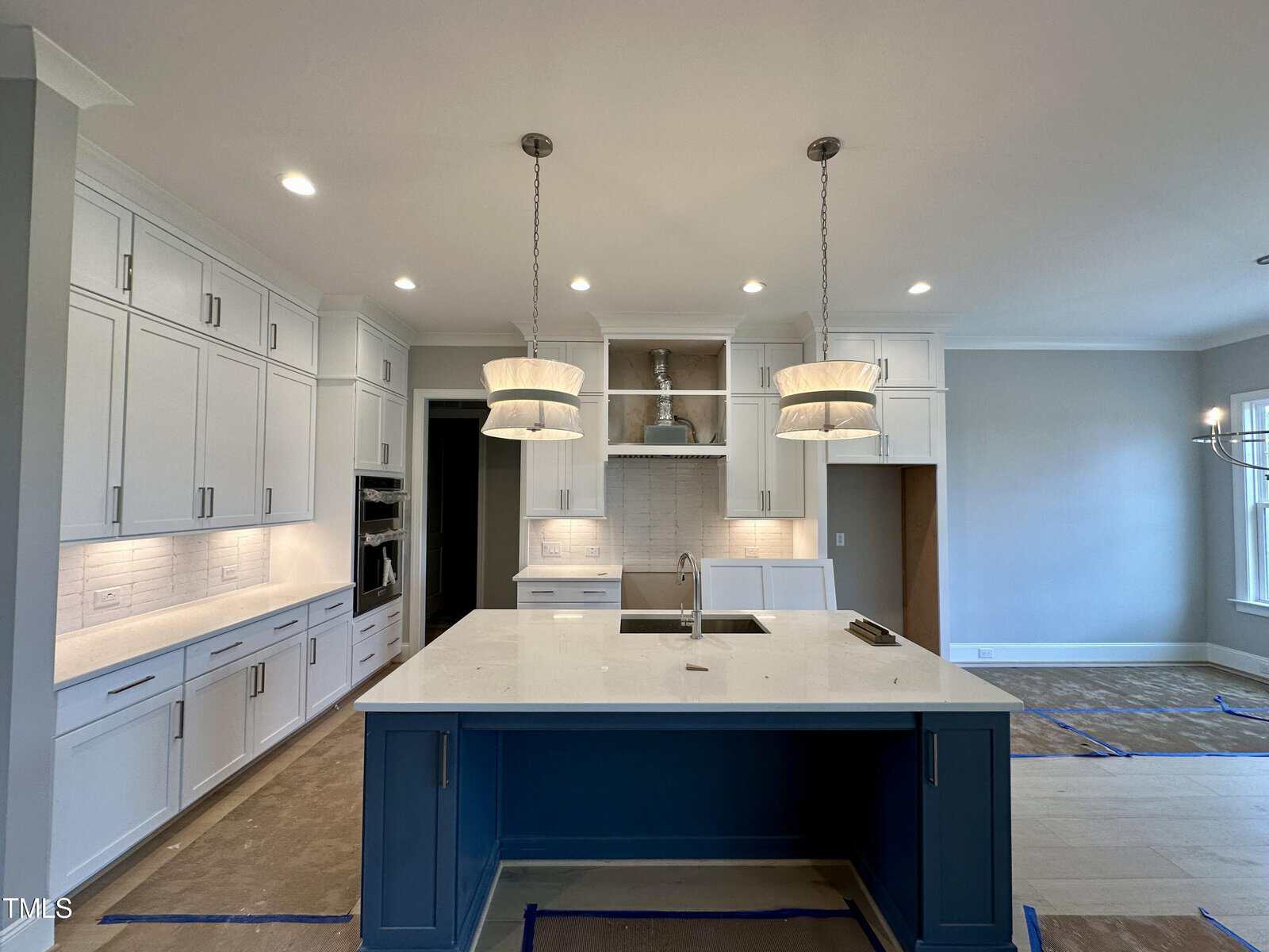 A modern kitchen with white cabinets, stainless steel appliances, and a blue island with a sink. Two pendant lights hang above the island, and recessed lighting is installed in the ceiling.