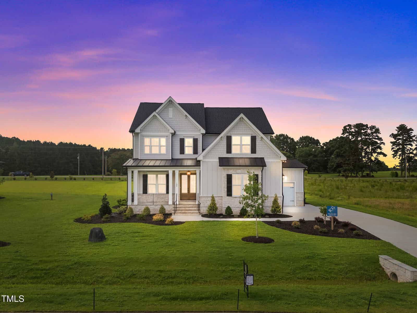 Two-story modern farmhouse at 190 Broadleaf Lane, Youngsville, with grey siding, black roof, and a front porch, sits on a manicured lawn at sunset beneath a vibrant purple and orange sky.