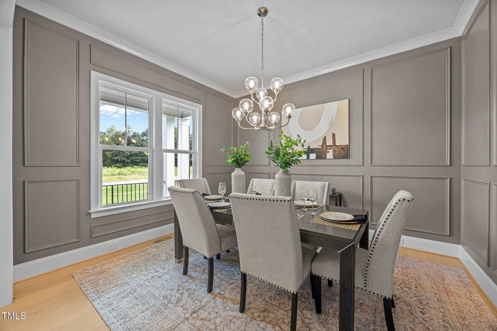 Elegant dining room with taupe paneled walls, a rectangular dark wood table set for six, upholstered chairs, contemporary chandelier, large window with outdoor view, and a neutral area rug on light wood floors.