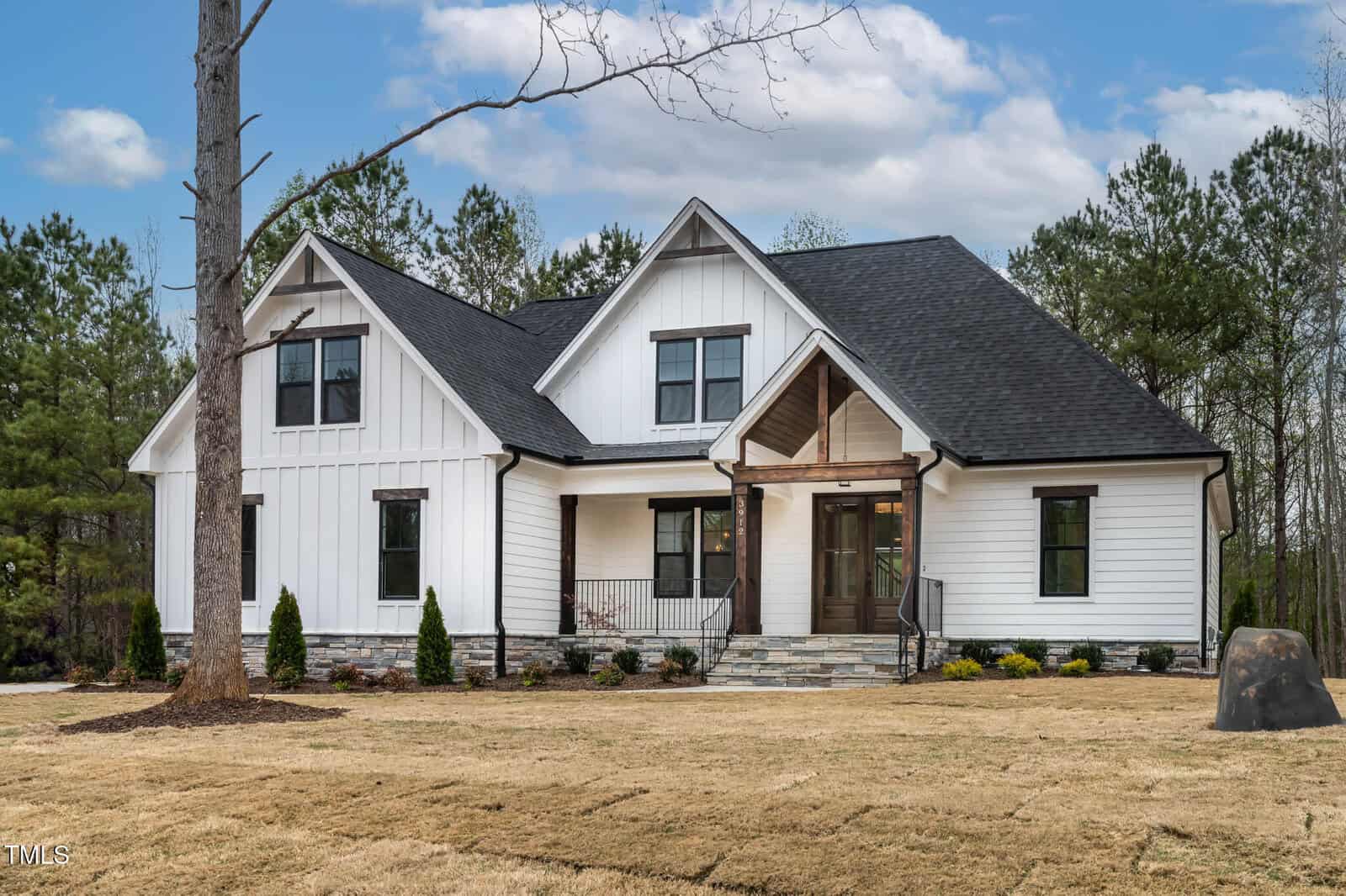Nestled at 3912 Cedar Knolls Drive in Youngsville, this white two-story house features a black roof, large windows, and a charming covered front porch. Stone steps lead to the entrance, surrounded by a neatly trimmed lawn and several small shrubs, with trees and a cloudy sky in the background.