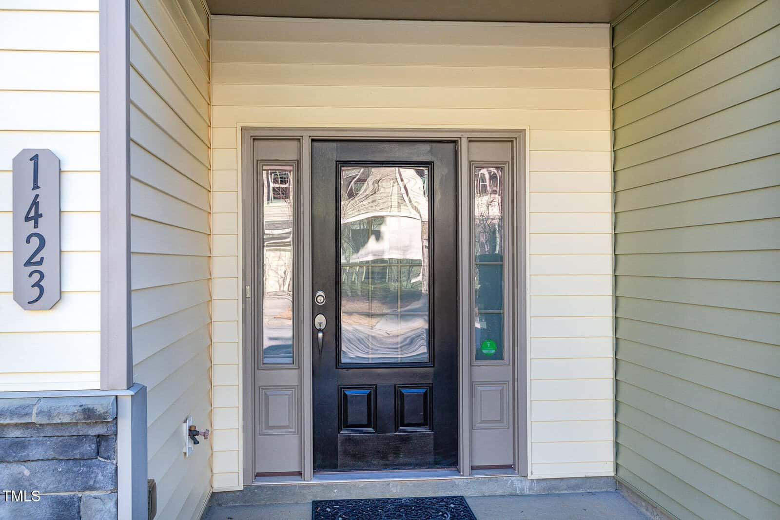 A front entrance with a black door featuring glass panels and sidelights, framed by cream-colored siding. The house number 1423 is mounted vertically on the left side.