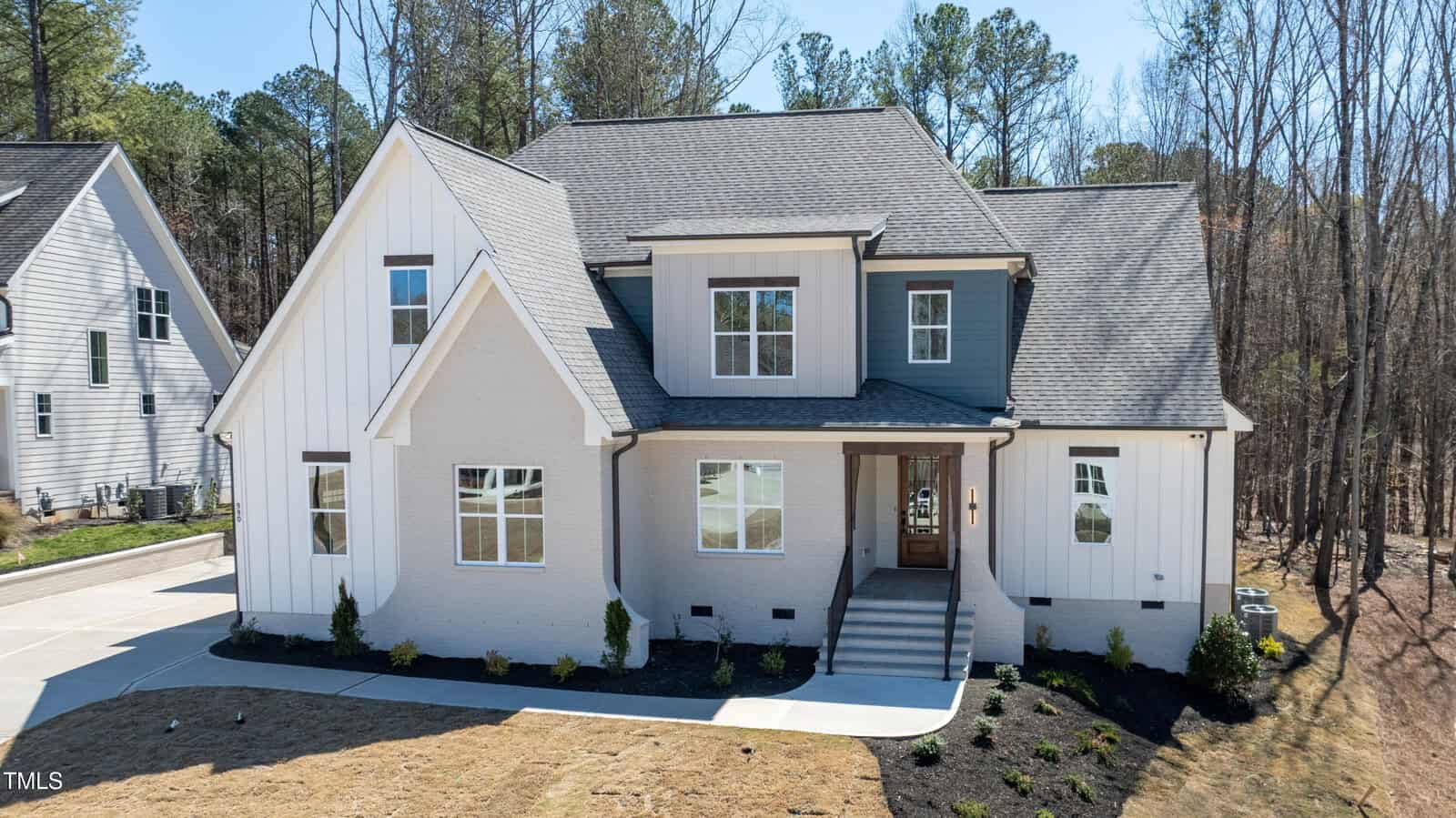 A modern, two-story house at 990 Browning Place in Youngsville features light gray brick and white vertical siding, large front windows, a covered entryway with steps, and a landscaped front yard in a wooded suburban neighborhood.
