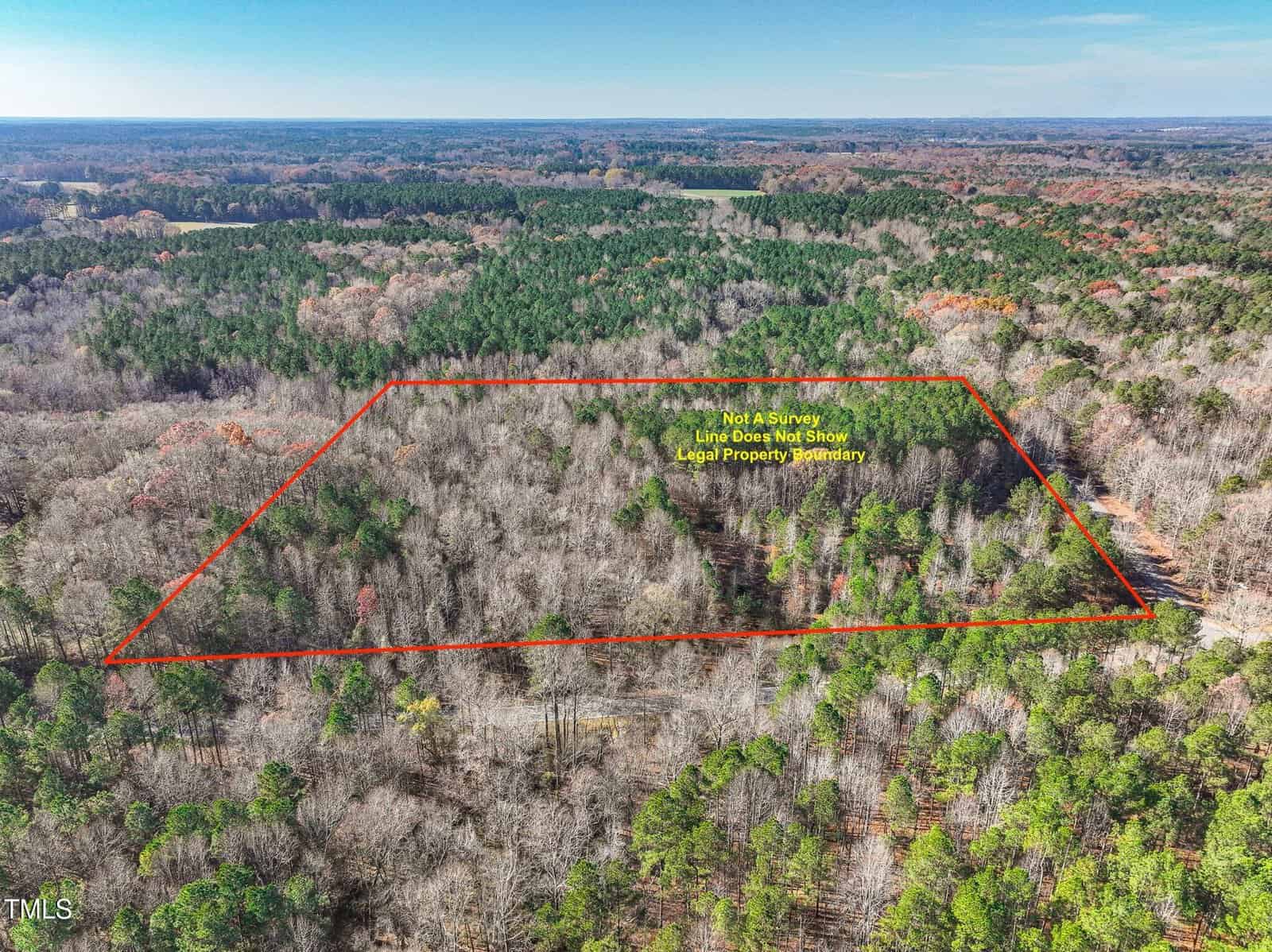 Aerial view of a rectangular plot of wooded land outlined in red, with a note stating "Not a Survey Line Does Not Show Legal Property Boundary." Surrounding area consists of dense forest and clear sky.