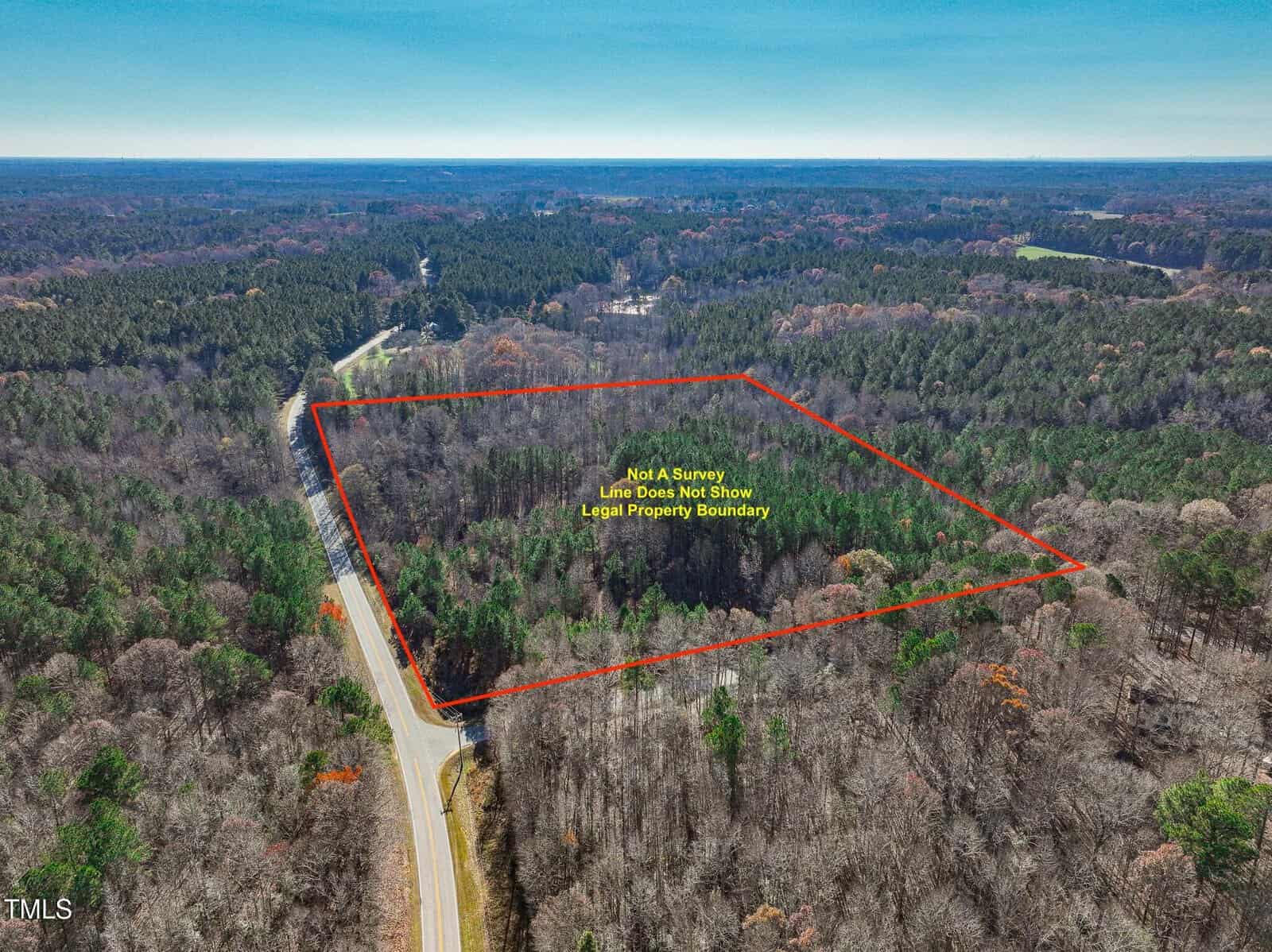 Aerial view of a wooded area with a road on the left. An orange line outlines a section of forest, labeled “Not A Survey, Line Does Not Show Legal Property Boundary.” Dense trees cover the outlined land.